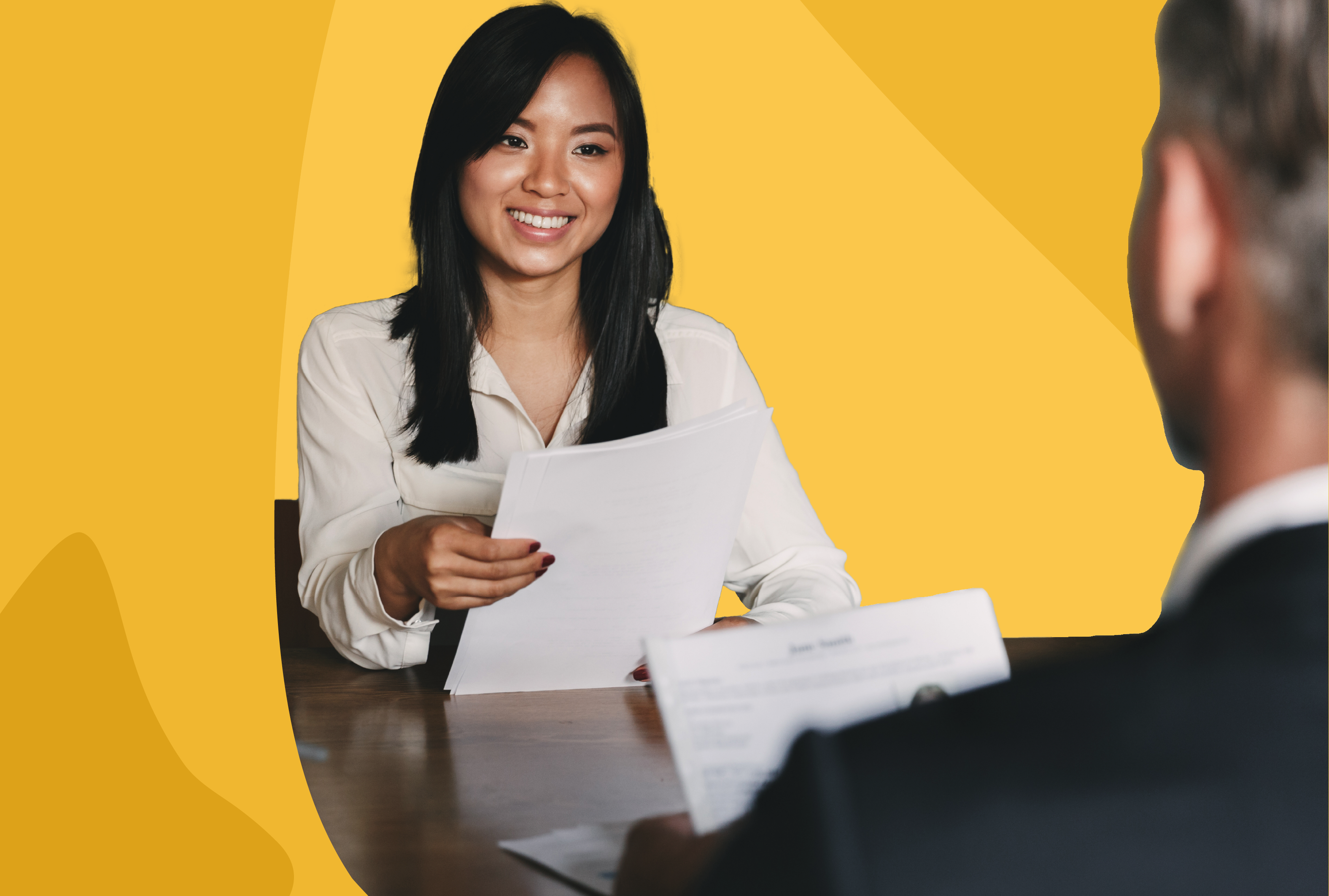 Woman dressed in white collar shirt holding paper and smiling at a table